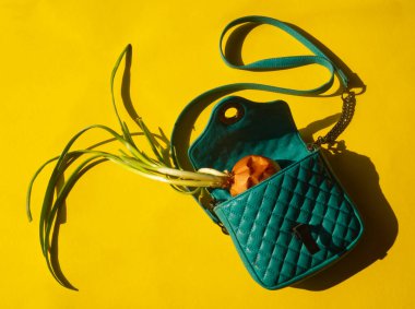 Sebze alışverişi konsepti. Sarı arka planda yeşil çantalı yeşil soğan. Benzin mavisi kadın çantasında sebze. Kopyalama alanı olan bir düzen. Market torbası yaratıcı fikri. Minimalist yaşam tarzı