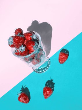 Pembe ve turkuaz arka planda cam bir fincanda kırmızı çilekler. Olgun kırmızı böğürtlenler. En az yiyecek ve meyve konsepti. Çapraz çizgiler ve geometrik yüzey.