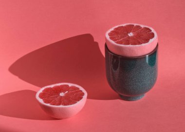 Olgun pembe dilimlenmiş greyfurt mavi seramik kasede pastel pembe arka planda. Citrus meyvesi. Modern yiyecek minimalist konsepti. Yemek hala hayattadır. C vitamini, antioksidan. Sert ışık, gölge, klasik konsept