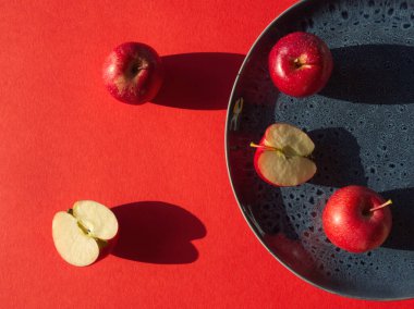Kırmızı arka planda mavi plakalı kırmızı elmalar. Kırmızı olgun meyve. Modern yiyecek minimalist konsepti. Yemek hala hayattadır. C vitamini, antioksidan, demir zengini yiyecekler. Mavi el seramik. Güneşli sırtta dilimlenmiş elmalar