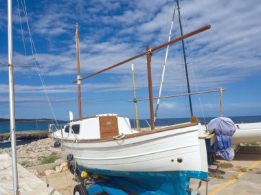 Deniz Burnu. Tekne limana yanaşıyor, deniz ve mavi gökyüzü arka planında. Rıhtım yakınlarında denizde yüzen küçük yelkenlilerin görüntüsü. Limanda eski bir tekne. Balearen, Mayorka, İspanya. Peyzaj