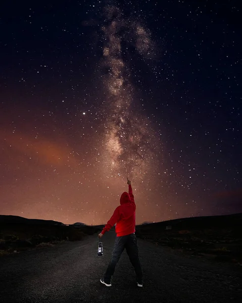 Man pointing to the milky way with his hand and a lantern in the other
