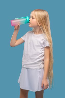 Beyaz elbiseli uzun saçlı kız su içiyor.