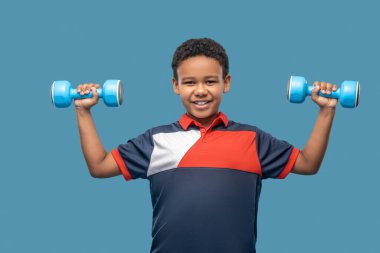 Koyu tenli mutlu çocuk, dambılları kaldırıyor.