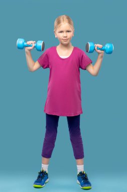 Spor kıyafetli kız ellerinde dambıllarla.