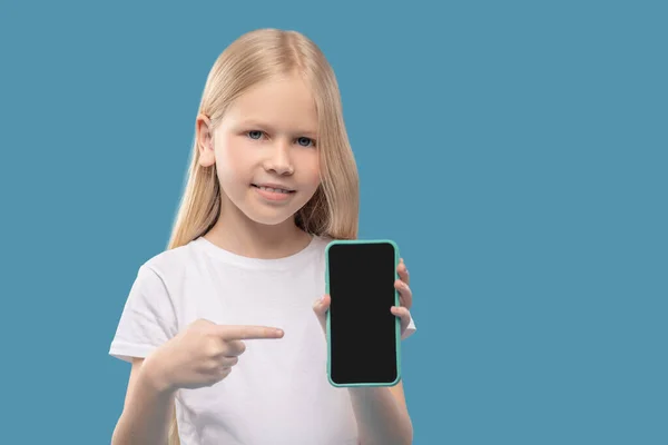 Chica alegre señalando con el dedo al teléfono inteligente en la mano — Foto de Stock