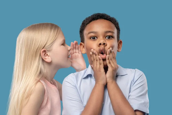 Chica diciendo secreto en el oído de chico sorprendido — Foto de Stock