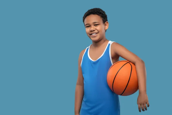 Africano americano menino feliz segurando bola no fundo azul — Fotografia de Stock