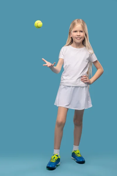 Girl standing tossing up tennis ball