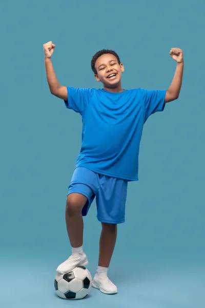 Niño con pelota de fútbol levantando las manos victoriosamente —  Fotos de Stock