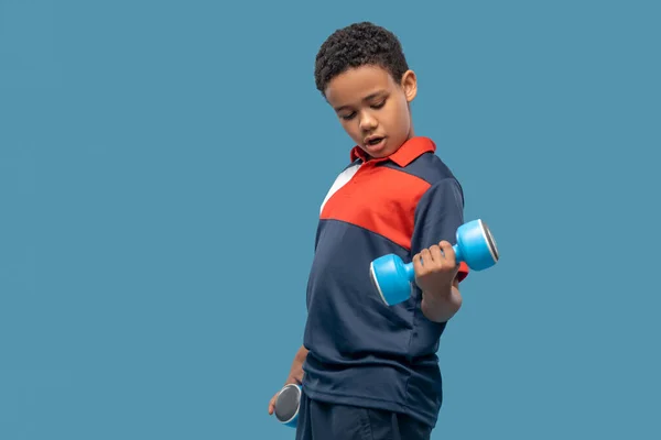 Dark skinned boy doing strength exercise with dumbbells — Φωτογραφία Αρχείου