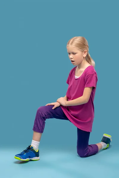 Flicka gör övningar stående på ett knä på golvet — Stockfoto
