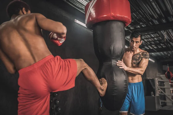 Spor salonunda egzersiz yapan ve kum torbasını tekmeleyen iki adam. — Stok fotoğraf