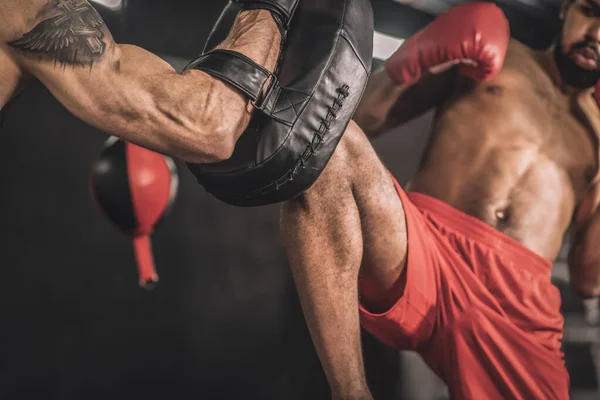 Jovem kickboxer de cabelos escuros trabalhando em seu chute na perna com um treinador — Fotografia de Stock