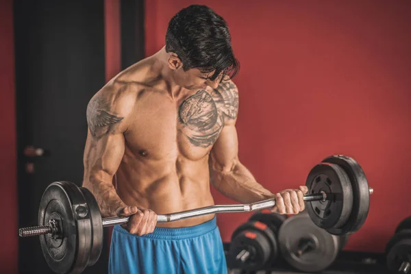Young man with a tattoo on a chest working with the barbells in a gym