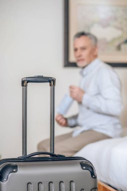 Otel odasında koruyucu maskeli, orta yaşlı, gri saçlı bir adam.