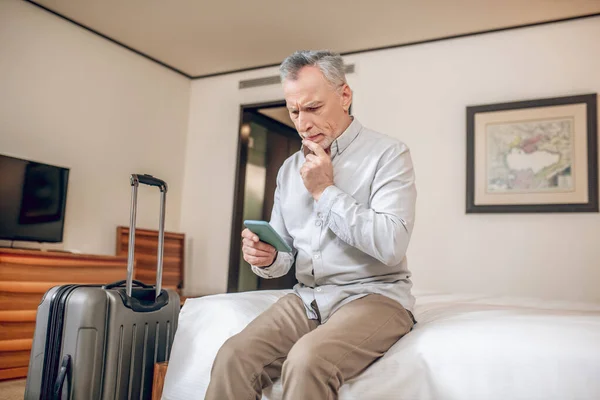 Oteldeki bir yatakta elinde akıllı bir telefonla oturan orta yaşlı bir iş adamı. — Stok fotoğraf