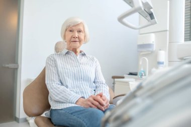 Kıdemli kadın dişçi muayenehanesinde oturup doktoru bekliyor.