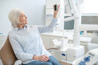 Gri saçlı kadın diş yenileme ameliyatından sonra selfie çekiyor ve memnun görünüyor.