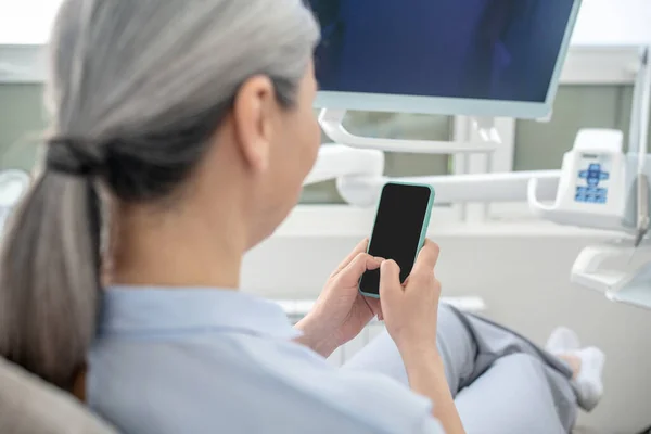 Kadın dişçi ofisinde oturuyor ve akıllı telefonuyla mesaj atıyor. — Stok fotoğraf