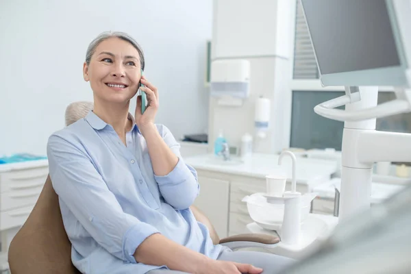 Mulher sentada no consultório de dentistas e falando ao telefone — Fotografia de Stock