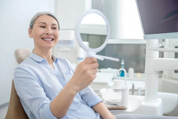 Mulher sentada no consultório de dentistas com um espelho nas mãos — Fotografia de Stock