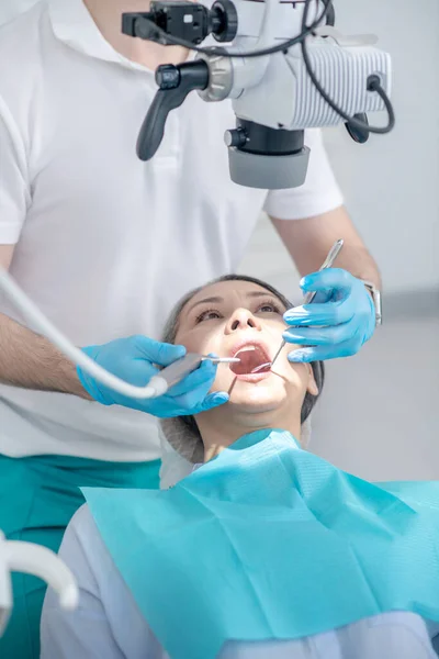 Cirurgião dentário masculino trabalhando com paciente e usando instrumento médico óptico — Fotografia de Stock