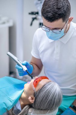 Gözlüklü kadın dişçi muayenehanesinde diş bakımı yaptırıyor.