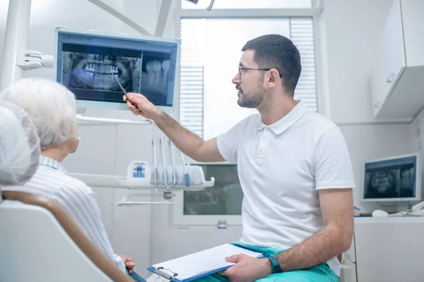 Homem jovem dentista explicando os resultados de xray para sua paciente do sexo feminino — Fotografia de Stock