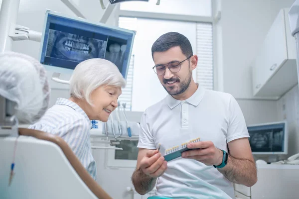 Homem jovem dentista escolhendo implante dentário com seu paciente — Fotografia de Stock