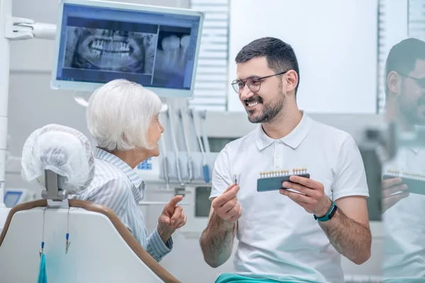 Hombre joven dentista elegir implante dental con su paciente — Foto de Stock
