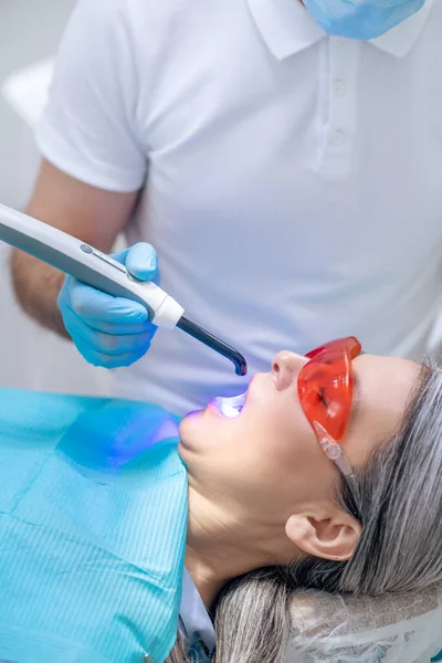 Mulher de óculos protetores com restauração dentária no consultório odontológico — Fotografia de Stock