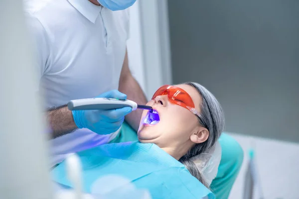 Mulher de óculos protetores com restauração dentária no consultório odontológico — Fotografia de Stock