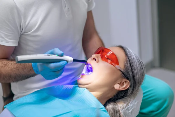 Vrouwelijke patiënt in beschermende oogkledij met een tandheelkundige restauratie bij de tandarts kantoor — Stockfoto