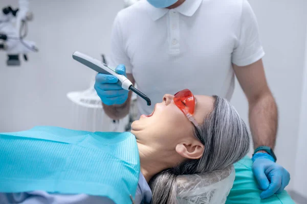 Vrouwelijke patiënt in beschermende oogkledij met een tandheelkundige restauratie bij de tandarts kantoor — Stockfoto