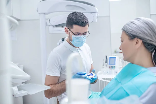 Jovem dentista mostrando uma dentadura para sua paciente do sexo feminino — Fotografia de Stock