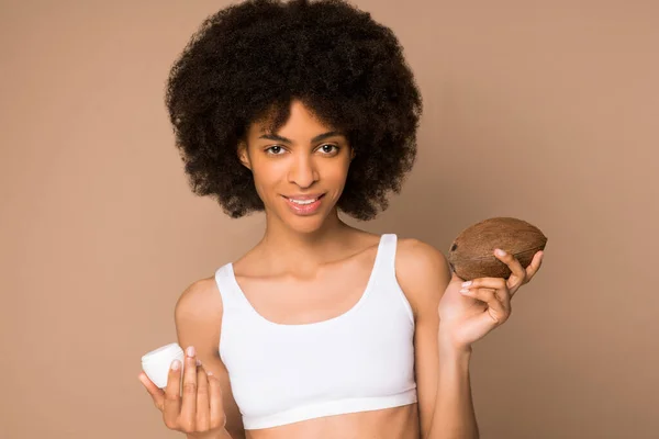 Una joven mulata de pelo rizado con un coco y un tarro de crema — Foto de Stock