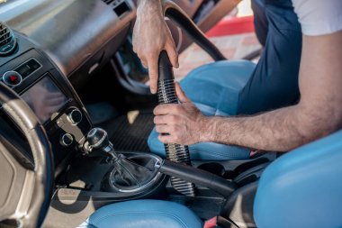 Ön koltukların yanında elektrikli süpürgeyle erkek eli.