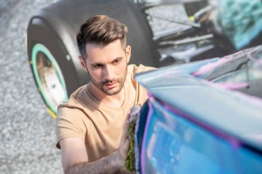 Çekici bir adam arabanın yüzeyini siliyor.