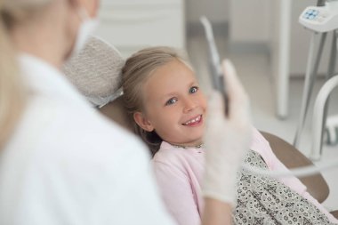 Sarışın bir doktor küçük hastasıyla çalışırken elinde diş matkabı tutuyor.