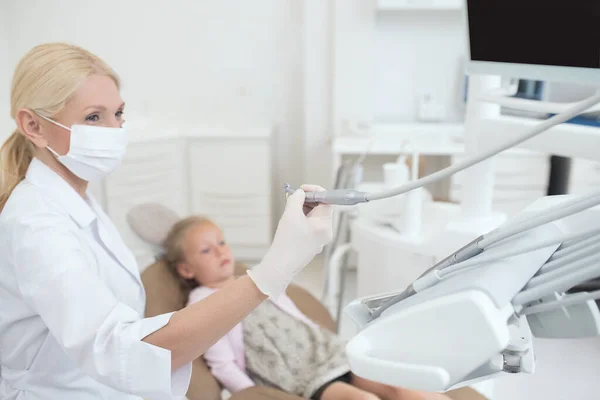 Um médico loiro segurando uma broca dentária enquanto trabalhava com seu pequeno paciente — Fotografia de Stock