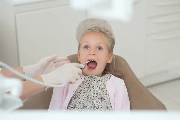 Um médico loiro segurando uma broca dentária enquanto trabalhava com seu pequeno paciente — Fotografia de Stock