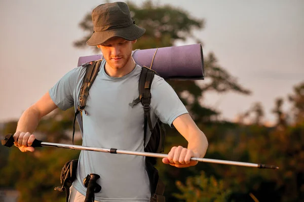 Ein junger Mann mit Rucksack steht auf dem Hügel, Wanderstöcke in der Hand — Stockfoto