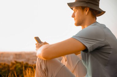 Tepede oturan şapkalı bir adam panoramik bir video çekiyor.