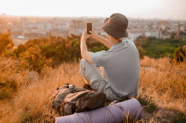 Tepede oturan şapkalı bir adam panoramik bir video çekiyor.