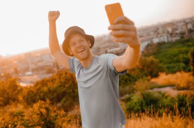 Tepede duran şapkalı bir adam selfie çekiyor.