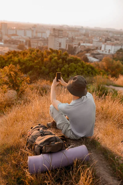 Tepede oturan şapkalı bir adam panoramik bir video çekiyor. — Stok fotoğraf