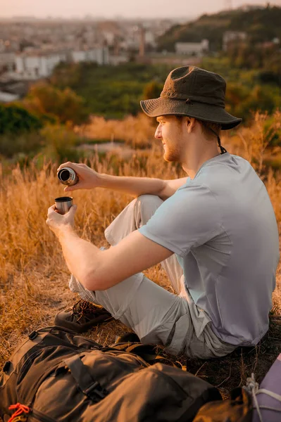 Ένας άντρας με καπέλο κάθεται στο λόφο και ξεκουράζεται. — Φωτογραφία Αρχείου