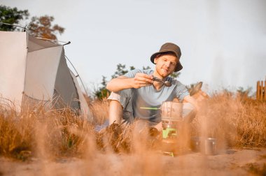 Bir erkek turist çadırının yanında kahvaltı yapıyor.