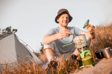 Bir erkek turist çadırının yanında kahvaltı yapıyor.